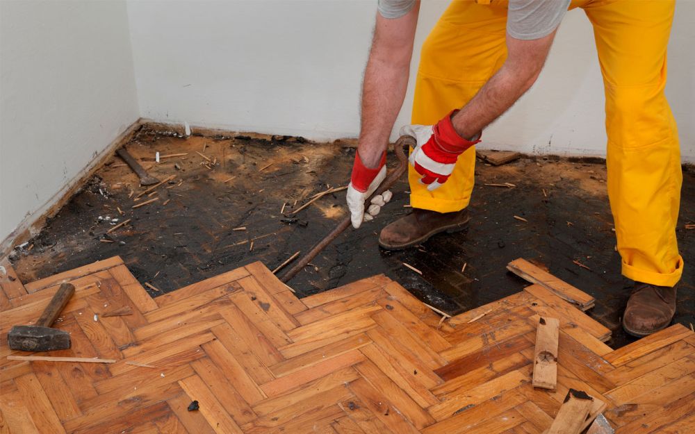 man using a pry bar to pull apart subfloor with water damage